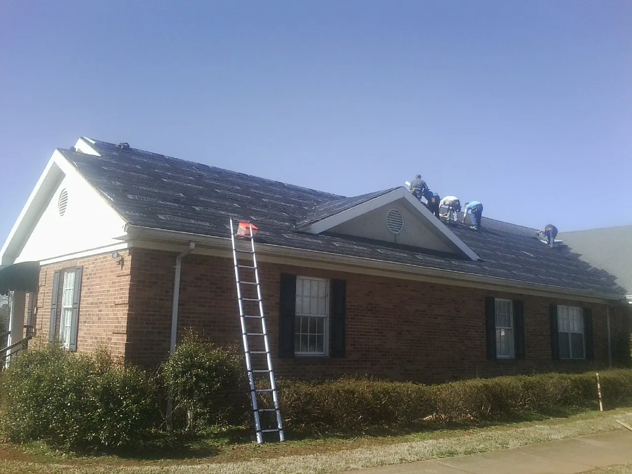 Crew tearing shingles off a brick ranch roof with a ladder set — Emergency Roof Repair work by our crew in Troy